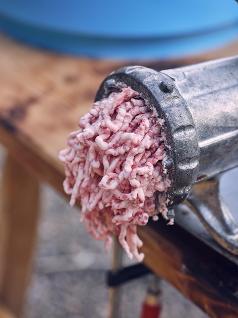 Processo de alto ângulo de preparação de carne fresca moída crua com moedor de metal envelhecido colocado sobre mesa de madeira em açougue tradicional