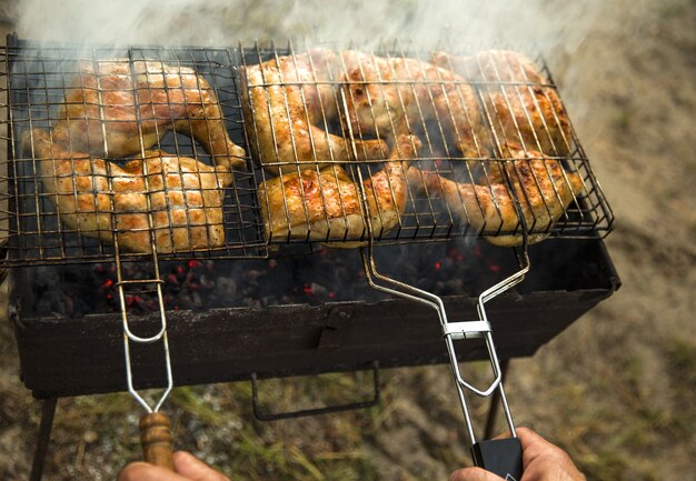 Processo de churrasco ao ar livre. O homem está fazendo grelha de frango. Está queimando com fumaça. Mãos masculinas estão segurando eles