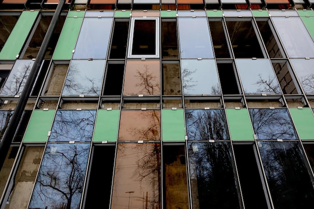 Processo de construção, envidraçamento de fachada de edifício residencial, hotel ou outro imóvel comercial. Janelas vazias e envidraçadas com reflexo de árvores.