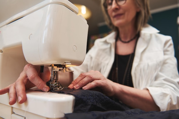 Processo de costura Detalhes de mãos femininas costurando tecido preto na máquina de costura profissional no local de trabalho Mãos de costureira segurando têxteis para produção de vestidos