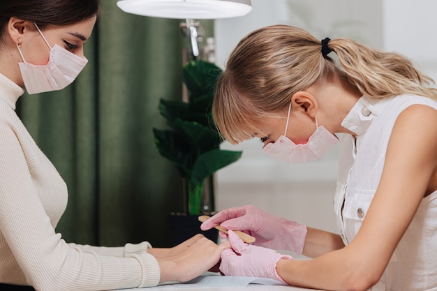 Processo de manicure. trabalhe em casa. o mestre faz uma manicure. duas mulheres com máscaras médicas.