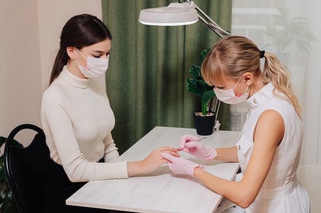 Processo de manicure. Trabalhe em casa. O mestre faz uma manicure. Duas mulheres com máscaras médicas.