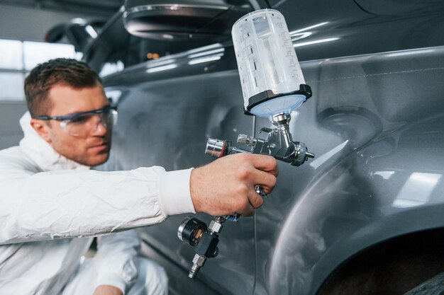 Foto processo de pintura do carro homem de uniforme está trabalhando no serviço de automóveis