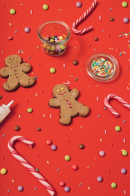 Processo de preparação do biscoito de gengibre de natal com homem-biscoito, glacê, granulado de açúcar e bastões de doces em um fundo de mesa vermelho. plano de papel de parede de ano novo lay.