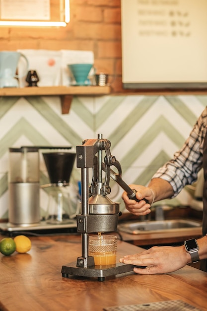 Processo de sumo. mãos masculinas preparando suco de laranja fresco pressionando a alavanca do espremedor mecânico em pé no balcão de bar no café