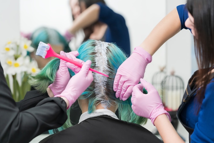 Processo de tingimento de cabelo em salão de beleza de dois cabeleireiros profissionais aplicando tinta no cabelo durante ...