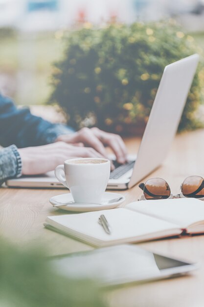 Processo de trabalho. Close de jovem trabalhando em um laptop enquanto está sentado em um café na calçada