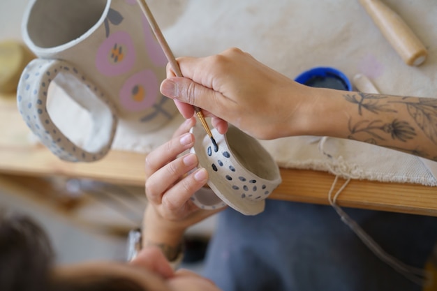 Processo de trabalho com ceramista de cerâmica decorando utensílios de cozinha de argila para loja de decoração artesanal
