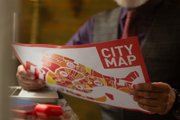 Procurando o caminho. Mapa da cidade brilhante nas mãos do visitante barbudo do café, sentado à mesa com seu laptop nele.