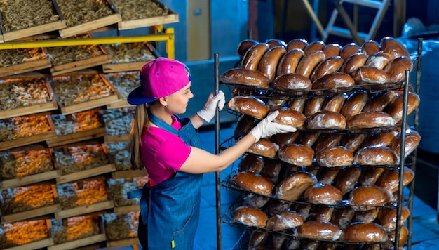 Produção de produtos de panificação Padeiro feminino olhando pães frescos na padaria