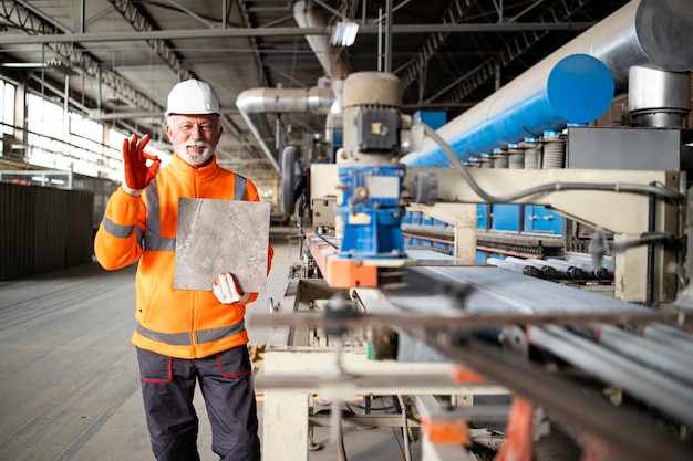 Producción exitosa de baldosas cerámicas y trabajador profesional de fábrica o empleado con chaqueta de alta visibilidad y casco que sostiene el producto.