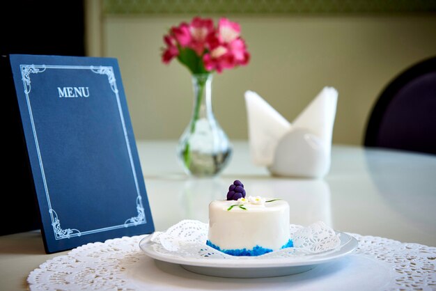 Un producto de confitería en un plato blanco con encaje está sobre una mesa con una disposición vacía del menú.