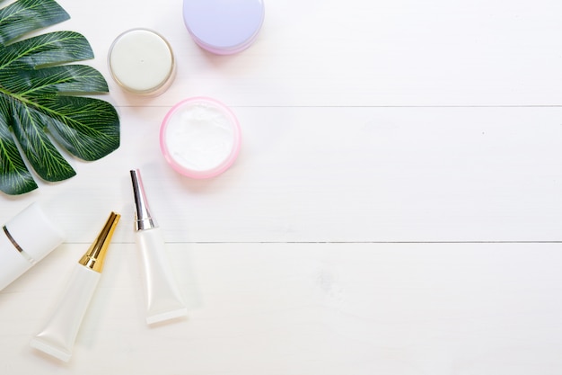 Producto cosmético y cuidado de la piel y hojas verdes en mesa de madera blanca.