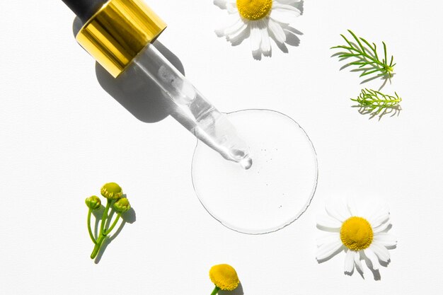 Producto cosmético líquido con gotero de vidrio sobre fondo blanco y flores de manzanilla medicinales