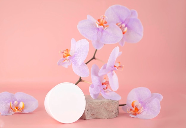 Producto para el cuidado de la piel Tubo de crema blanca sobre piedra de travertino junto a una flor de orquídea en un diseño de fondo rosa claro La crema o loción cosmética es un producto hecho a mano para el cuidado de la piel Cosméticos naturales exóticos
