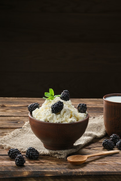 Producto lácteo, requesón y leche en un tazón de cerámica marrón con cuchara sobre madera