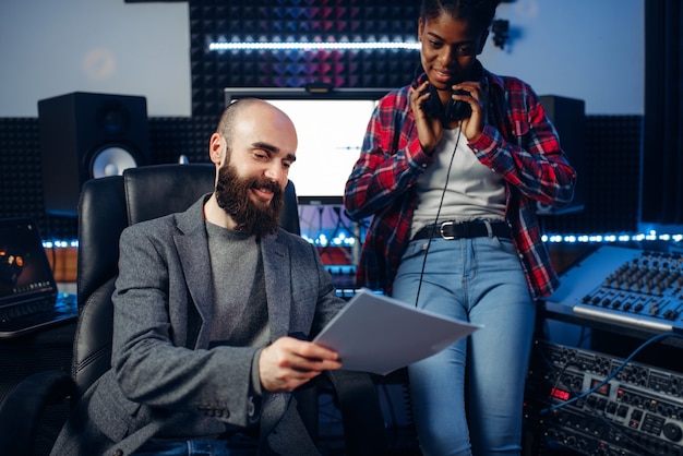 El productor de sonido masculino y la cantante en auriculares escucha la composición en el estudio de grabación. Tecnología profesional de mezcla de audio y música