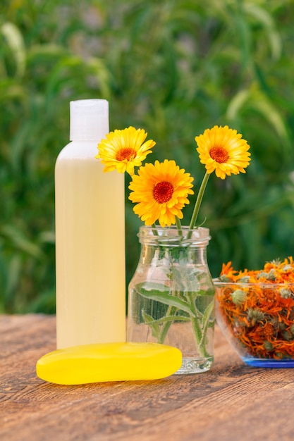 Productos y accesorios de spa. Flores de caléndula en un frasco de vidrio y botella con producto para el cuidado de la piel, con extracto de caléndula, recipiente con flores secas de caléndula sobre tablas de madera. Poca profundidad de campo