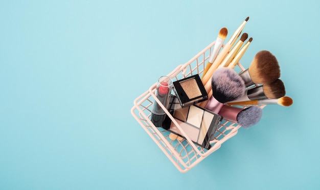 Foto productos de belleza de maquillaje en la canasta de la compra sobre un fondo azul