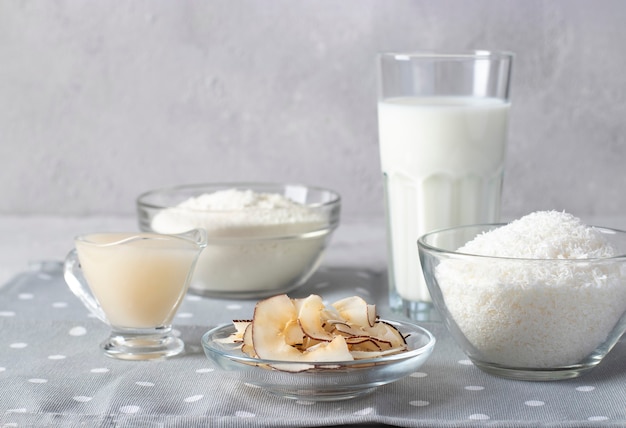 Productos de coco: copos de coco, harina, leche, leche condensada y patatas fritas sobre fondo gris claro. Alimentación saludable