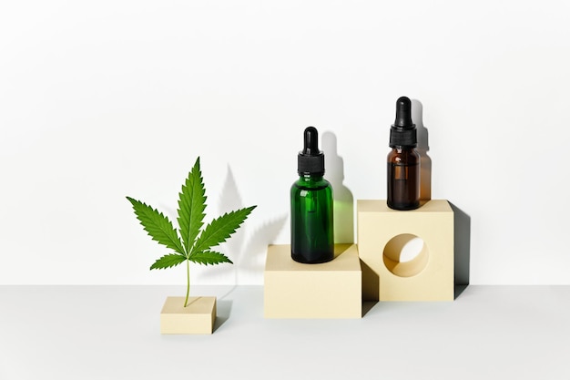 Productos cosméticos con aceite de CBD y extracto de cáñamo Botellas de vidrio y hojas de cáñamo en podios geométricos abstractos con sombras de moda