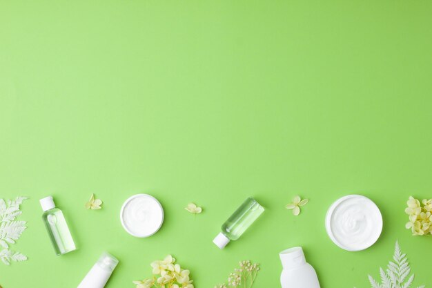 Productos cosméticos para el cuidado de la piel con con flores sobre fondo verde espacio de copia plana