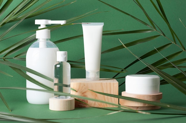 Productos cosméticos para el cuidado de la piel con podio de madera y hoja de palma sobre fondo verde Cerrar espacio de copia