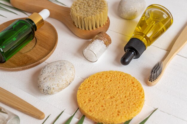 Productos cosméticos naturales SPA, composición con botellas de aceites esenciales, sal marina, esponjas, cepillos y herramientas de masaje sobre fondo blanco. Concepto de desperdicio cero