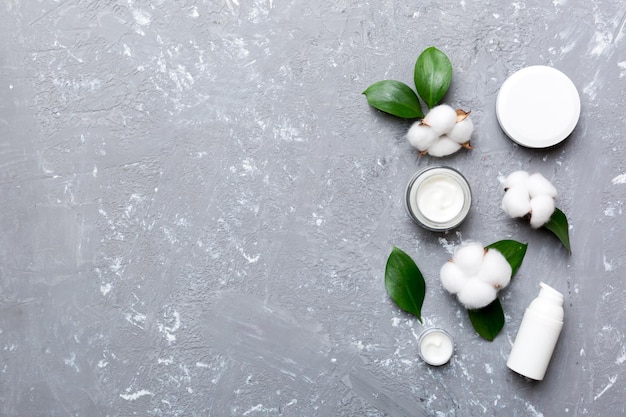 Productos cosméticos orgánicos con flor de algodón y hojas verdes sobre fondo de cemento. Copie el espacio, endecha plana.