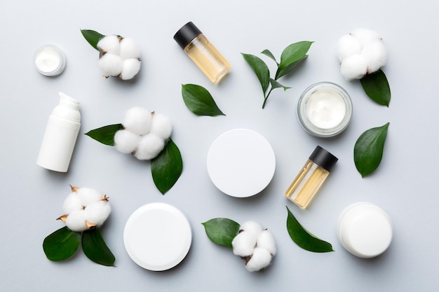 Productos cosméticos orgánicos con flor de algodón y hojas verdes sobre fondo de color Lay Flat