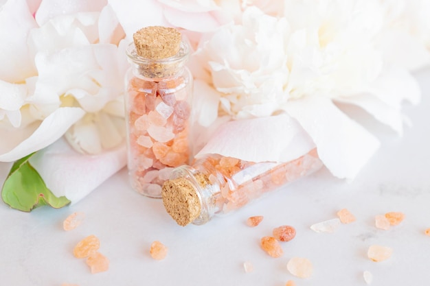 Productos cosméticos orgánicos naturales con flores de peonías rosas sobre fondo blanco Spa relax Tratamientos y masajes anticelulíticos Cosméticos naturales de belleza para baño spa sal rosa del himalaya