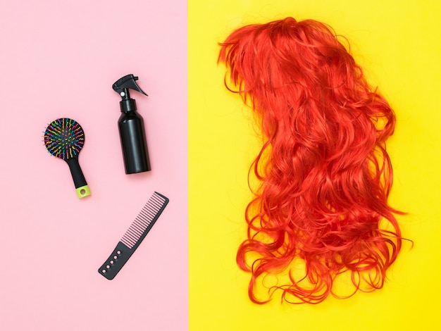 Productos para el cuidado del cabello y una peluca naranja brillante en una pared de dos tonos. Estilo de vida. Accesorios para crear estilo.