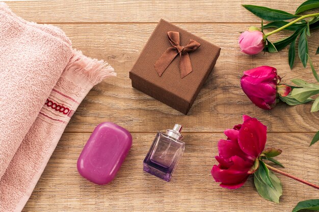 Productos para el cuidado facial y corporal. Caja de regalo, perfume, toalla suave con jabón y flores de peonía en el fondo de madera. Set de spa y cuidado corporal. Concepto de saludos de vacaciones. Vista superior.