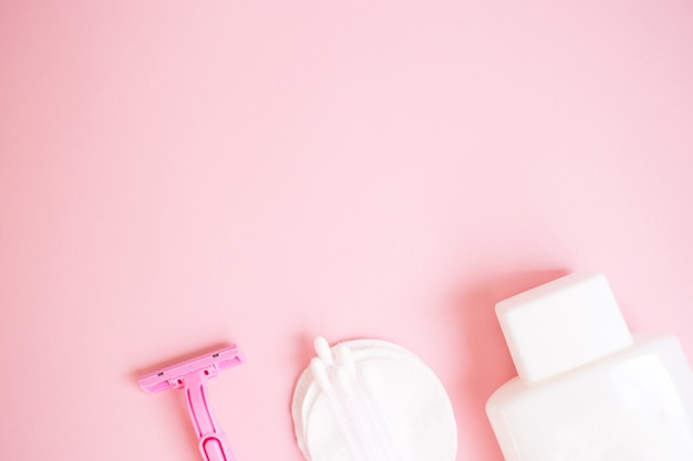 Foto productos de cuidado personal. botella blanca, maquinilla de afeitar, palillos para las orejas, almohadillas de algodón sobre fondo rosa. do