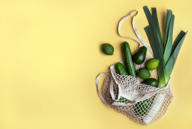 Productos ecológicos en una bolsa de malla reutilizable sobre un fondo amarillo.