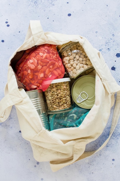 Productos enlatados de alimentos no perecederos en bolsa de algodón ecológico Nueces lentejas frijoles garbanzos y alimentos enlatados sobre un fondo azul