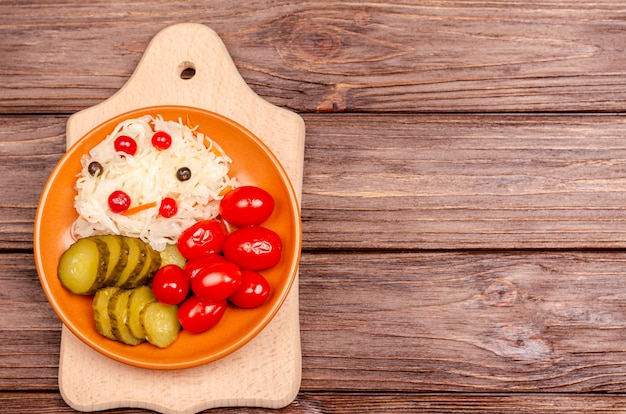 Productos fermentados caseros en un plato - chucrut, tomates, encurtidos en una tabla de madera