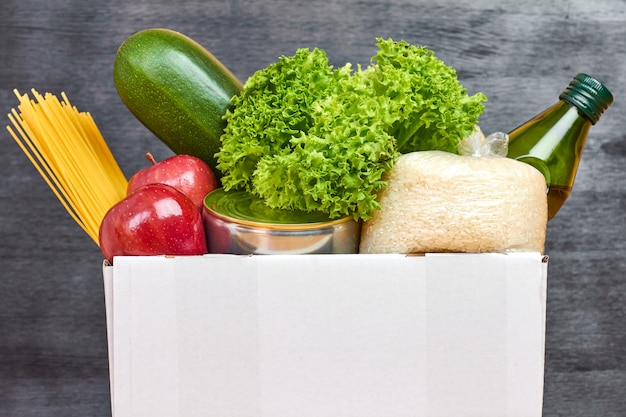 Productos frescos en una caja de donación en una pared negra. Entrega de comida en tienda online. Concepto de caridad.