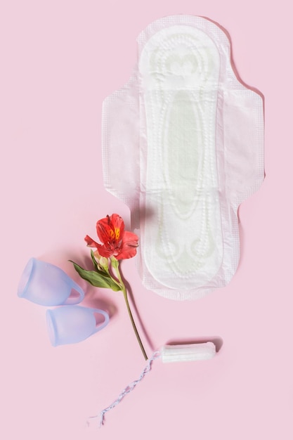 Productos de higiene menstrual que incluyen almohadillas de copa y un tampón en una vista superior de fondo rosa