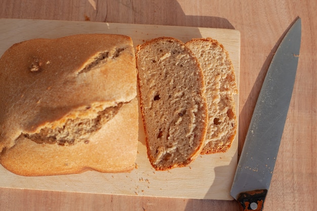 Productos horneados caseros. El panecillo está recién horneado en una tabla de cortar, cortado en rodajas con un cuchillo grande.