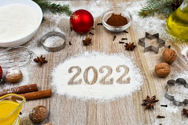 Productos para hornear galletas navideñas caseras sobre un fondo de madera con la inscripción 2022.