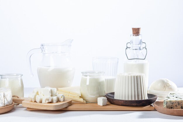 Foto productos lácteos en recipientes de vidrio y platos de madera sobre fondo blanco.