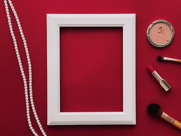 Productos de maquillaje de maqueta de marco de arte vertical blanco y joyas de perlas sobre fondo rojo como impresión de arte de diseño plano o concepto de álbum de fotos