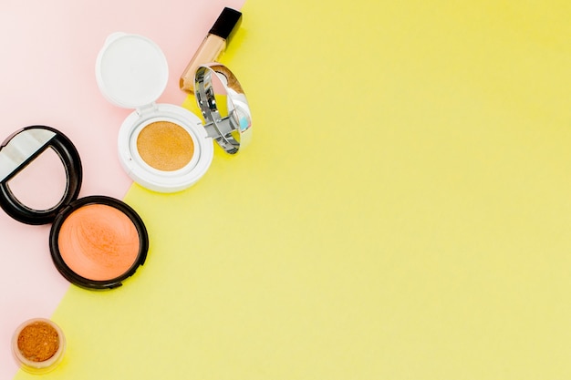 Productos de maquillaje que se derraman sobre un fondo amarillo y rosa brillante con espacio de copia, estilo minimalista