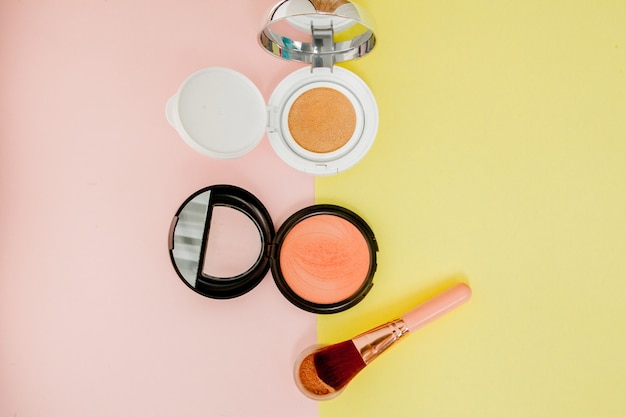 Productos de maquillaje que se derraman sobre un fondo amarillo y rosa brillante