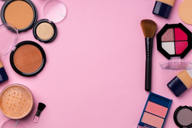 Productos de maquillaje para tez y pincel sobre rosa