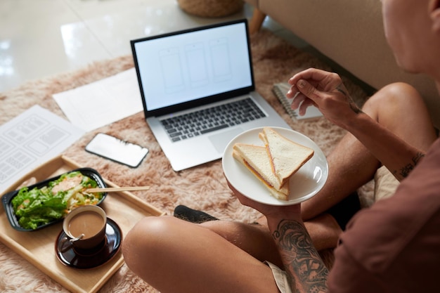 Produktmanager für Homewear beim Mittagessen und Überprüfung von Wireframes und Mockups auf neue Anwendungen