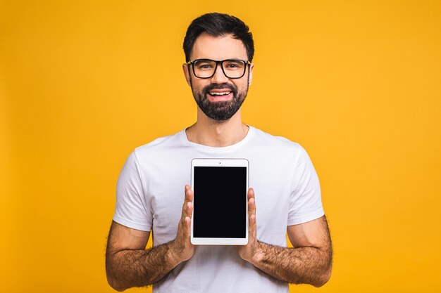 Produktpräsentation. Beförderung. Junger bärtiger Mann, der in Händen Tablet-Computer mit leerem Bildschirm hält, nah oben. Isoliert über gelbem Hintergrund.