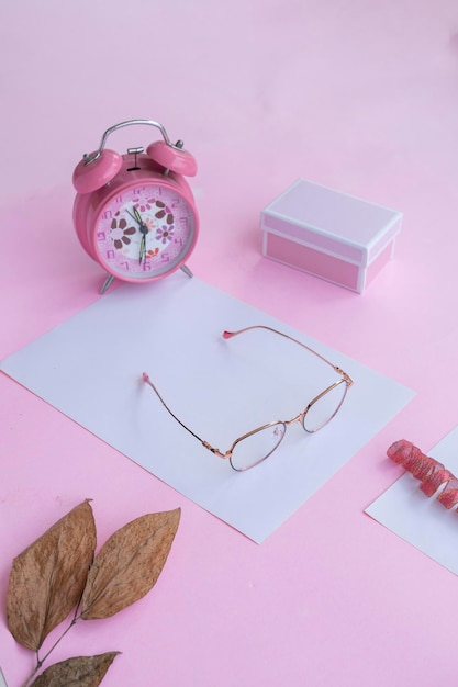 Produktpräsentation der minimalistischen Konzeptidee, quadratische Brille, Geschenkbox, Uhr und trockene Blätter auf rosafarbenem Papierhintergrund