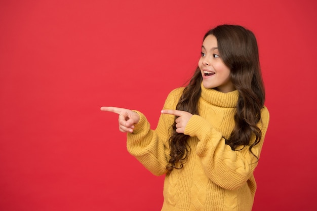 Produktpräsentation. Schau hier. Lockiges Haar stylen. Friseur Tipp. Langes gesundes glänzendes Haar des Kindermädchens. Natürliche Locken. Kind süßes Gesicht lockige Frisur. Kleines Mädchen wachsen lange Haare. Teenager-Mode-Modell.